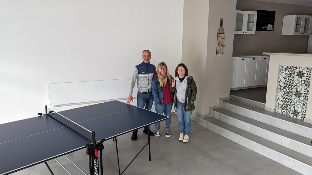 Mann und zwei Frauen stehen neben einer Tischtennisplatte